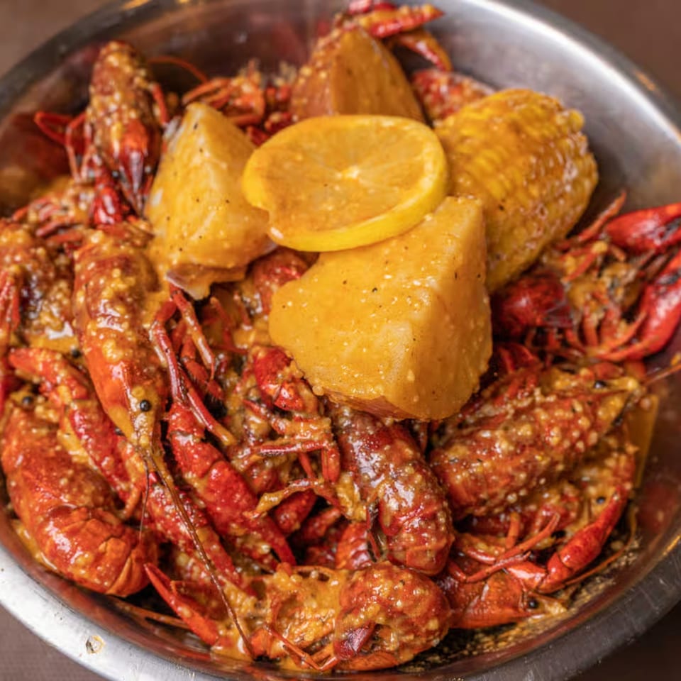 King Cajun Crawfish seafood boil with crawfish, potatoes, corn, and lemon slices in a metal bowl.