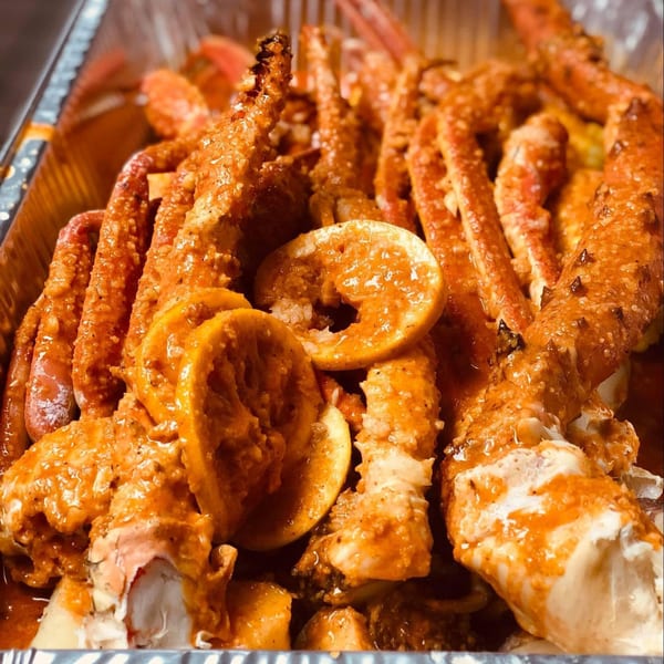 King Cajun Crawfish's crab legs and shrimp covered in sauce with lemon slices in a foil pan.