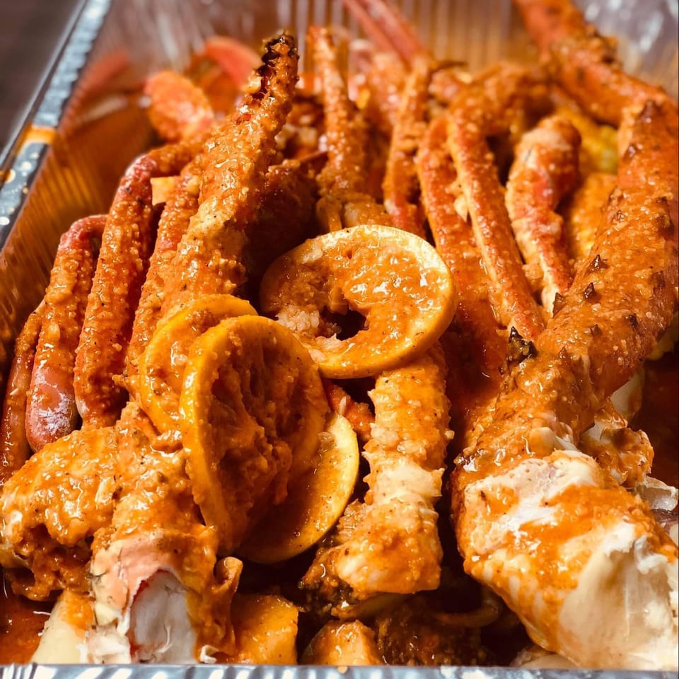 King Cajun Crawfish's crab legs and shrimp covered in sauce with lemon slices in a foil pan.