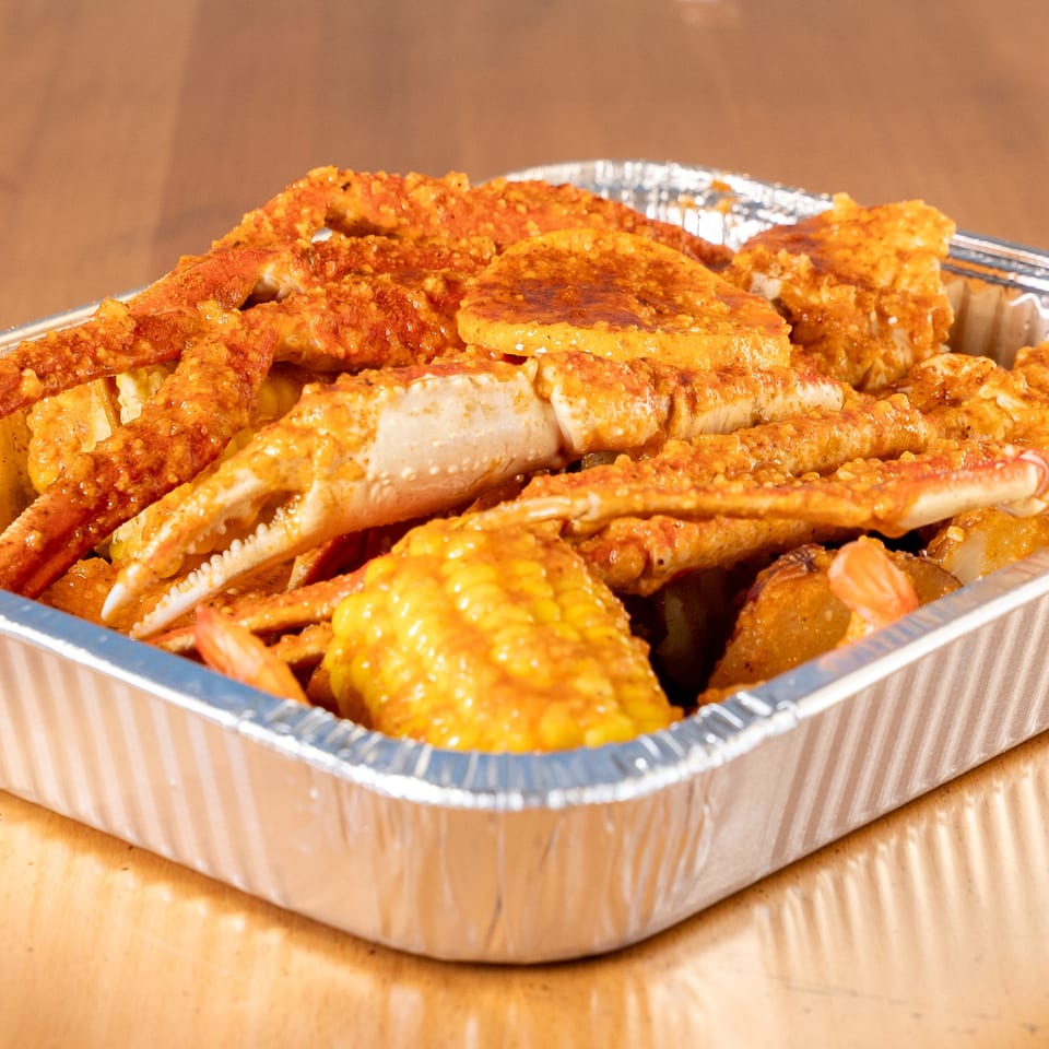 King Cajun Crawfish seafood boil with crab legs, corn, and potatoes in a foil pan.