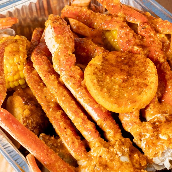 Close-up of King Cajun Crawfish's seafood boil with crab legs, corn, and potatoes in a spicy sauce.