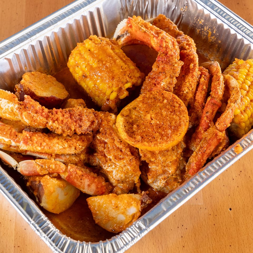 King Cajun Crawfish seafood boil with crab legs, corn, potatoes, and lemon in a foil pan.