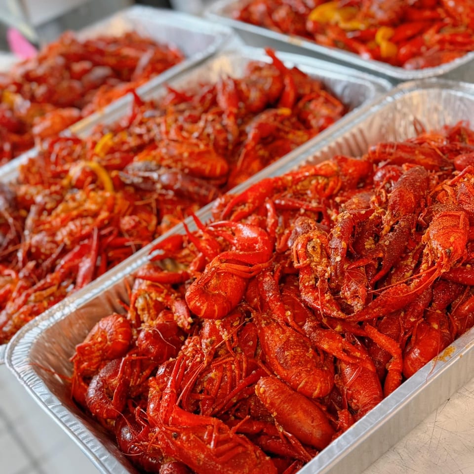 Multiple foil trays filled with bright red, seasoned King Cajun Crawfish, ready to be served.