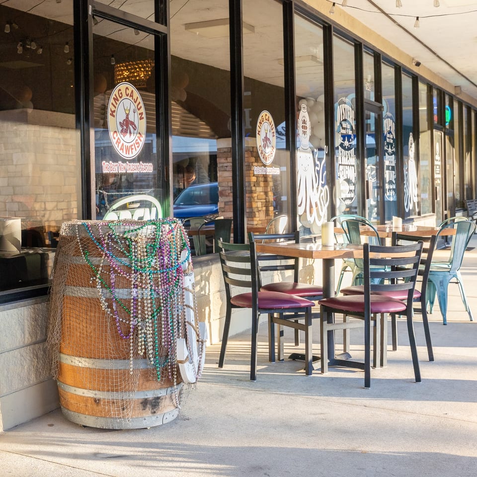 King Cajun Crawfish restaurant exterior with outdoor seating, a decorative barrel, and window decals.